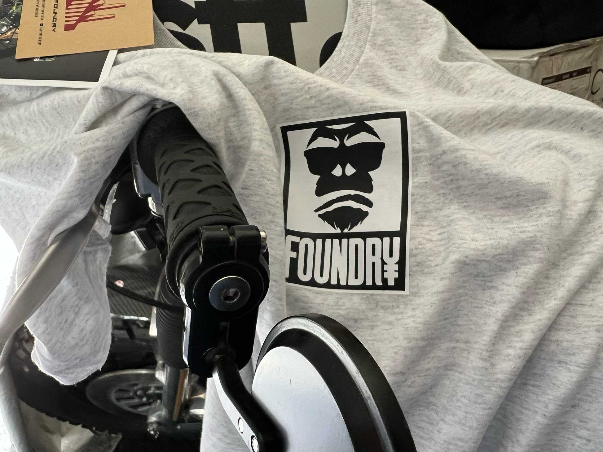 Gray t-shirt with 'Foundry' logo on a bike handlebar